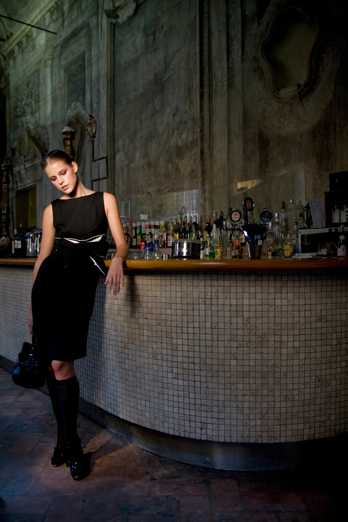 Modella in abito nero appoggiata al bancone di un bar